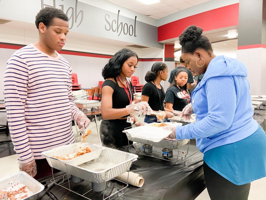 Sophomores Phillip Strange and Kim Ume-Ezeoke serve chicken to parent Lola Aje at Taste of Soul on Feb. 28. The event was held by the Black History Club to share traditional soul food with students and staff.