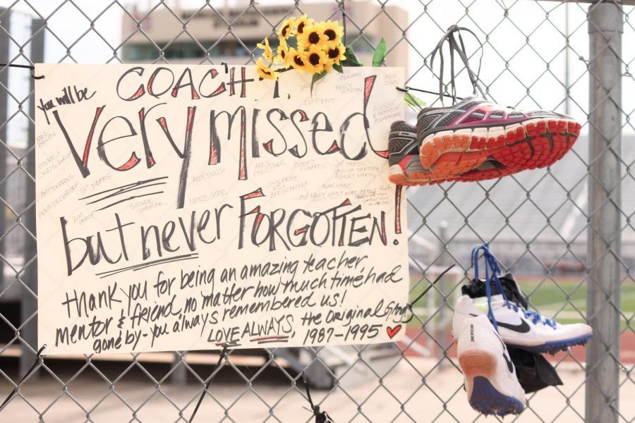 A note and shoes from some of the first athletes Head Cross Country, Track and Field Coach Steve Telaneus taught hang on the fence outside of the track to honor his memory.