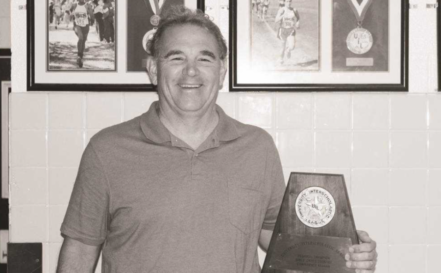 Head cross country, track and field coach Steve Telaneus poses with the girls cross country team's regional trophy in 2016.