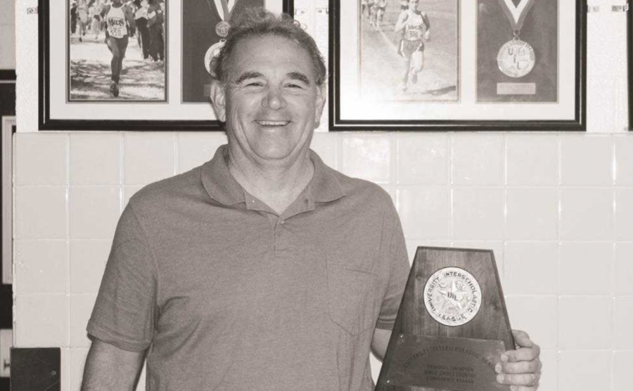 Head cross country, track and field coach Steve Telaneus poses with the girls cross country teams regional trophy in 2016.